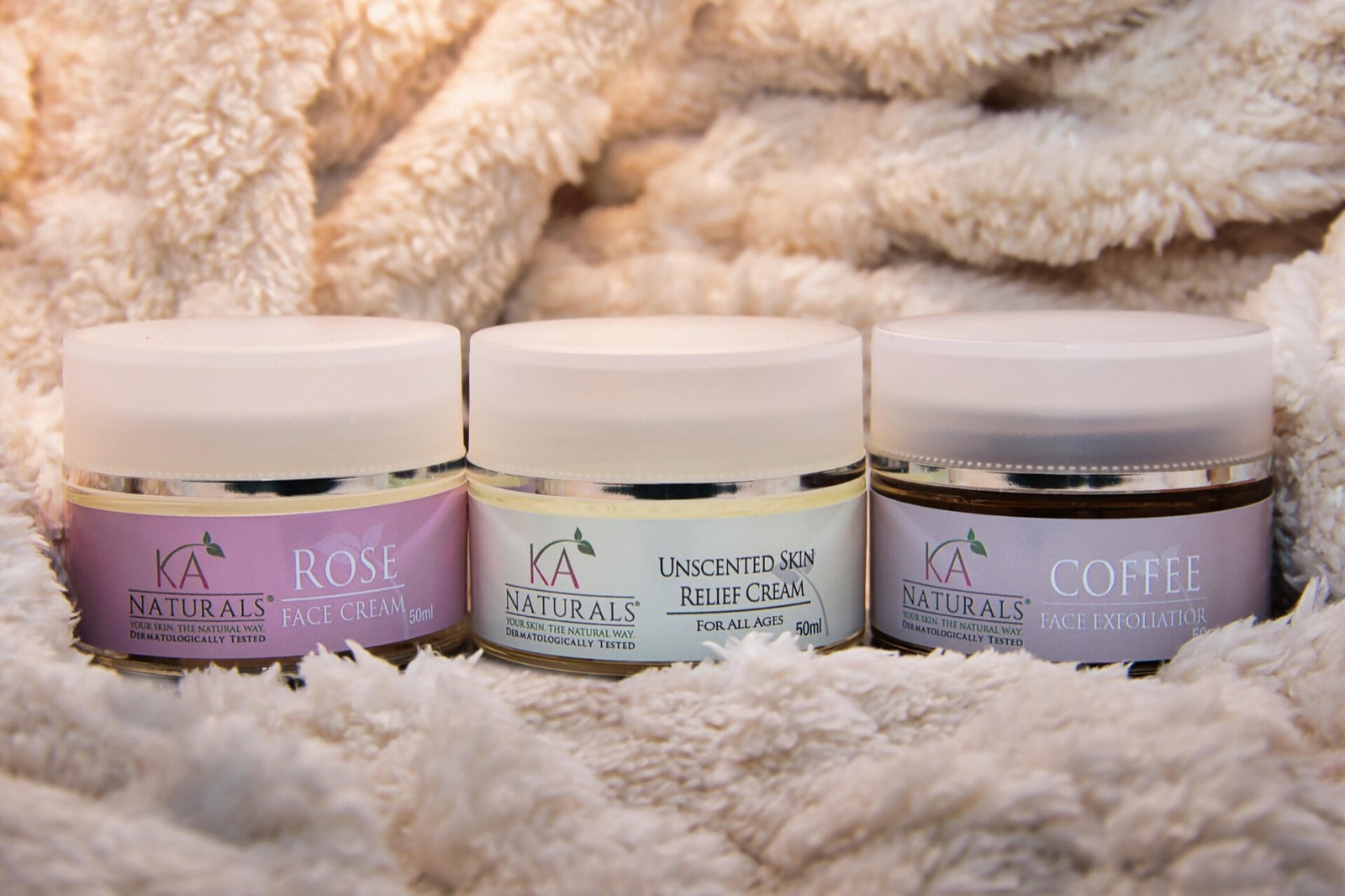 Three skincare jars on a soft cream blanket